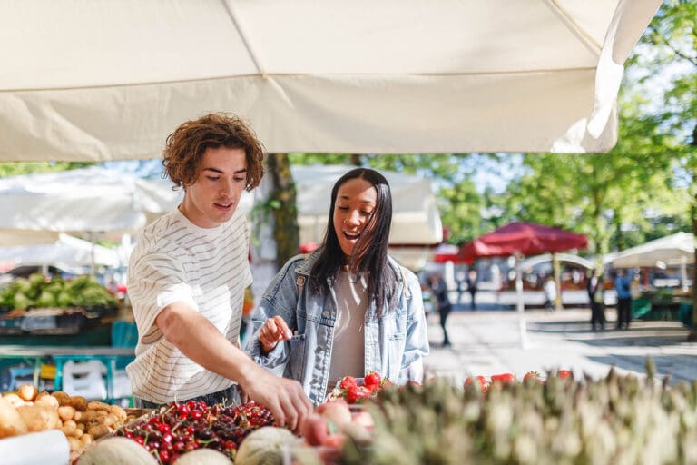 Happy multiethnic couple to shop fresh produce at an outdoor farmers' market. Concepts of joy, love, and togetherness.