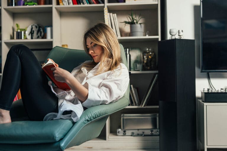 A smiling Caucasian female resting in her living room while enjoying reading a book.